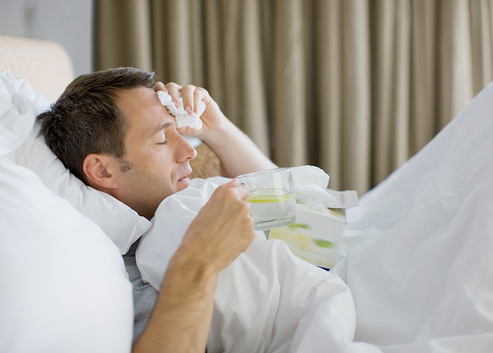 a man with cold sweats in bed drinking tea