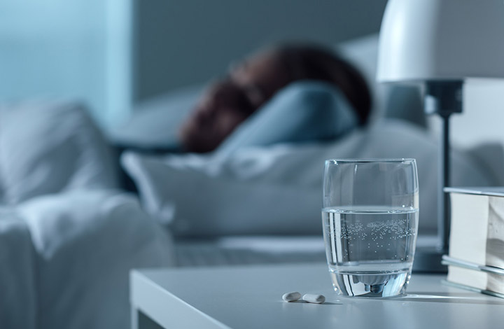 A woman sleeps with a water glass and pills on her bedside table