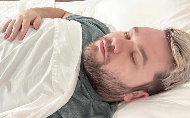 A man rests on his back while using the Quince Sateen Sheets.