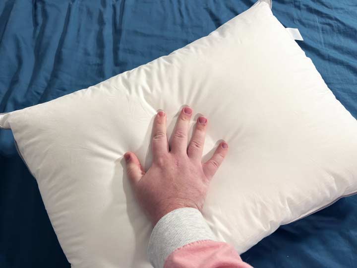An image of a hand placed on top of the cover of the Tuft & Needle Down Alternative pillow.