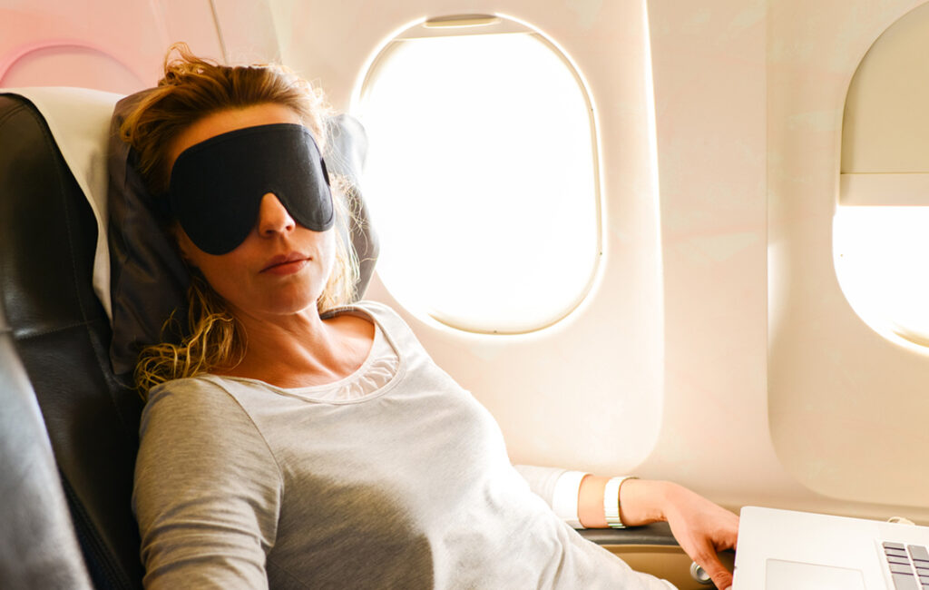woman sleeping on a plane with a sleep mask and pillow