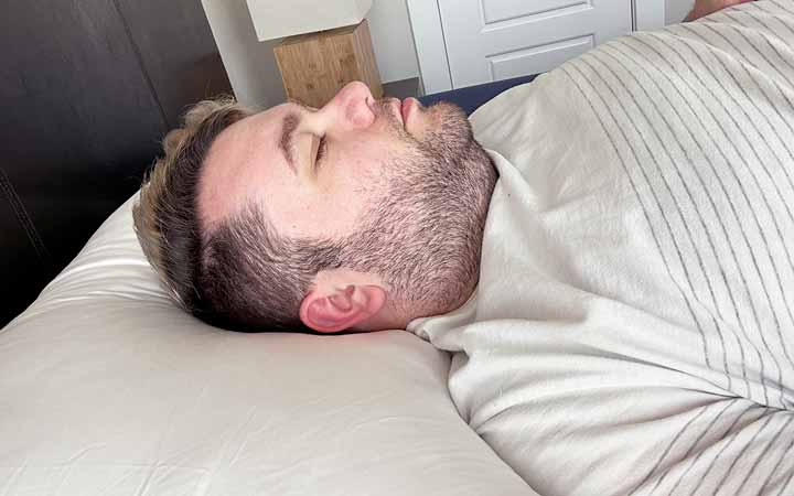 An image of a man sleeping on his back while using the Cozy Earth Silk Pillow.