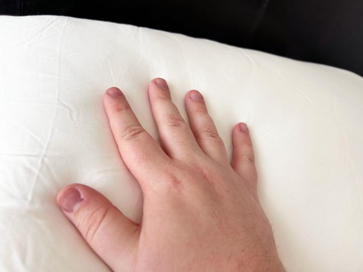 An image of a hand brushing across the Cozy Earth Silk Pillow cover.