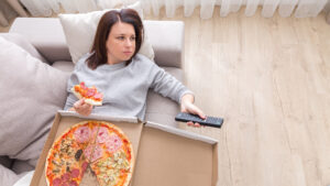 A woman eats pizza while laying on a couch