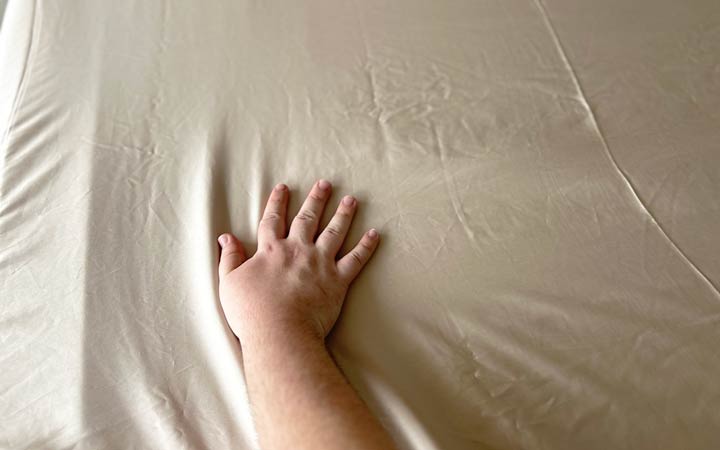 A hand brushes across the Ettitude Bamboo sheets.