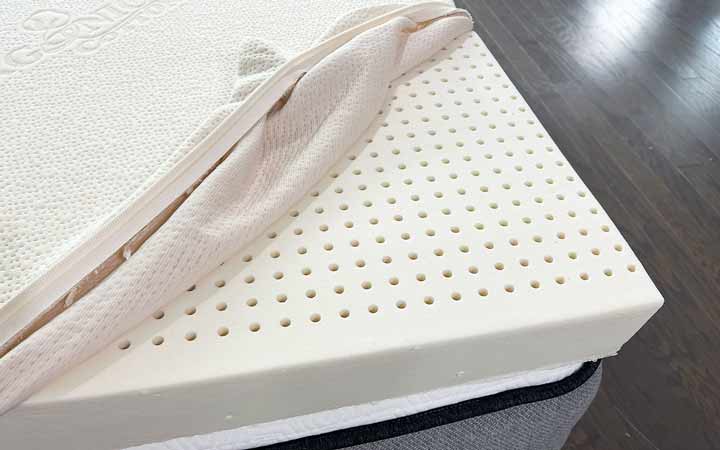 An image of the corner of the Plushbeds Latex topper, with the cover pulled back to reveal the perforated latex foam.