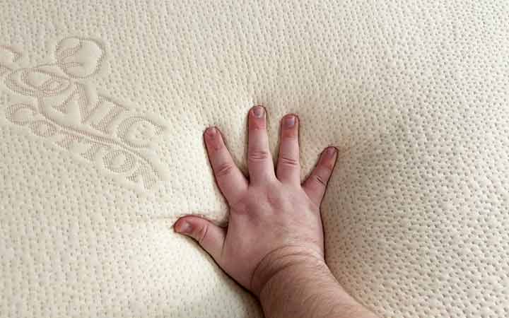 A hand presses into the Plushbeds Latex topper.