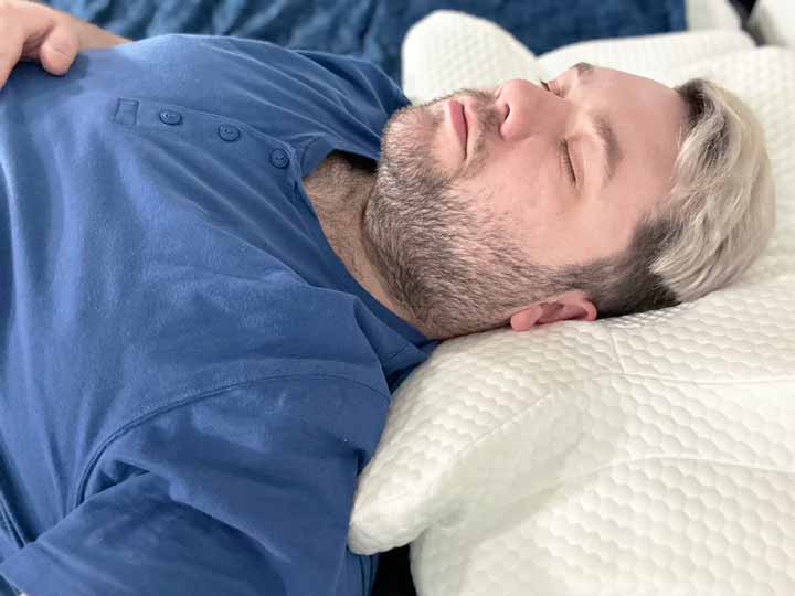 A man sleeps on his back while resting on the Zamat Butterfly Cervical Pillow.