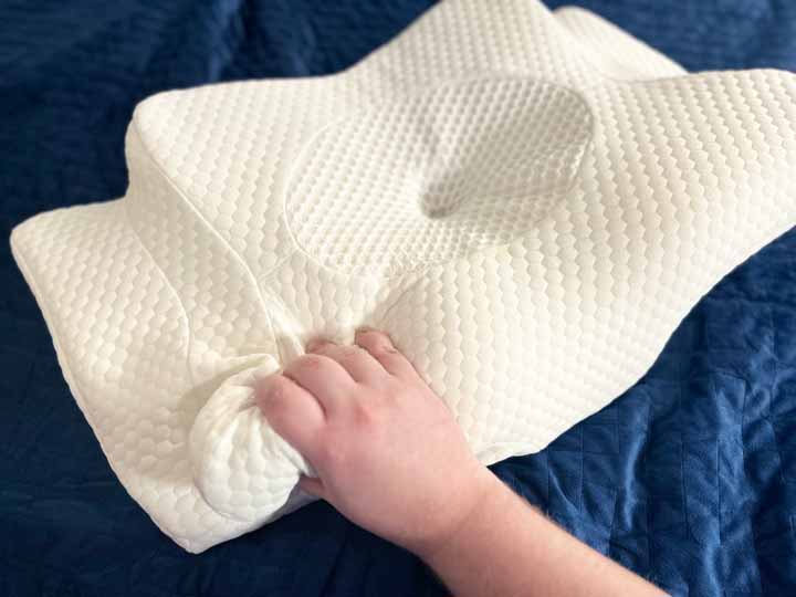 A hand squeezes the Zamat Cervical Butterfly pillow.