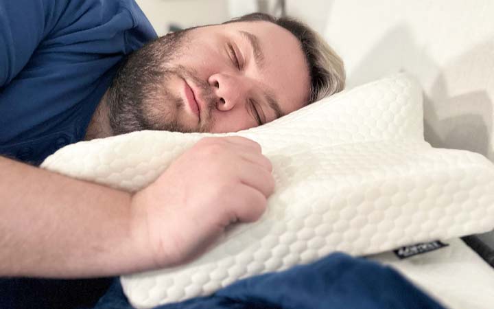 A man sleeps on his side while using the Zamat Butterfly Cervical Pillow.