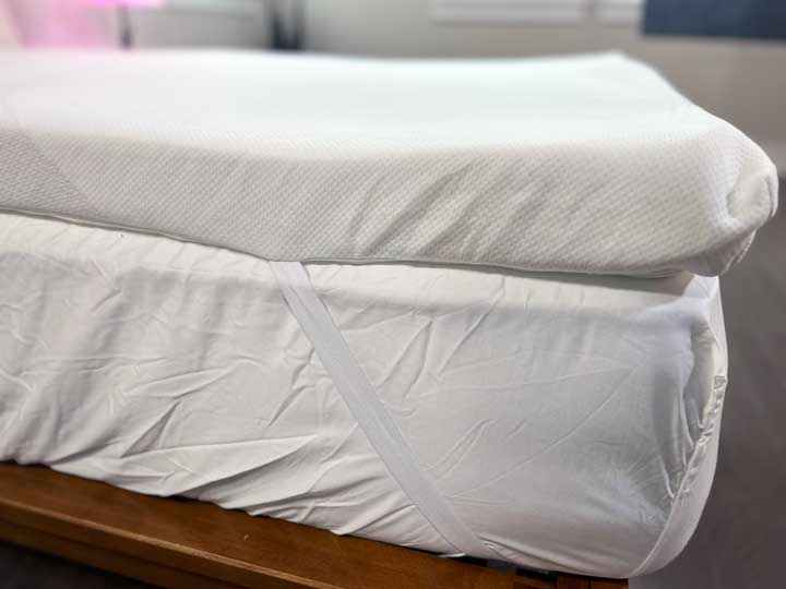 A side view of the TEMPUR-Adapt mattress topper, showing its height and the corner straps that attach it to the mattress.