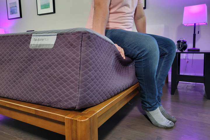 A man sits near the edge of the Purple RestorePlus mattress