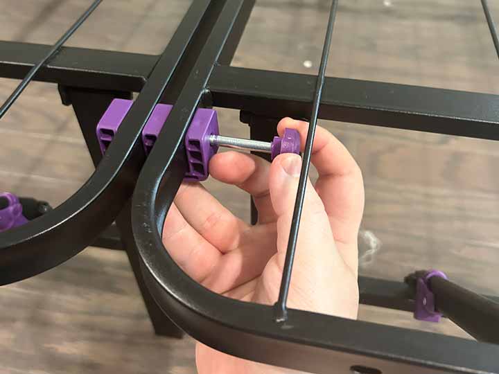 A hand screws in the Purple Platform bed frame with the plastic attachment.