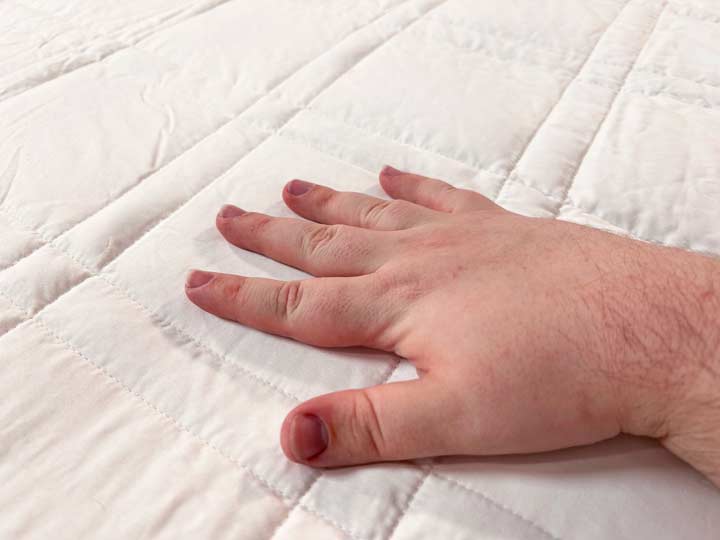 A hand runs across the smooth top of the Baloo Weighted Blanket.