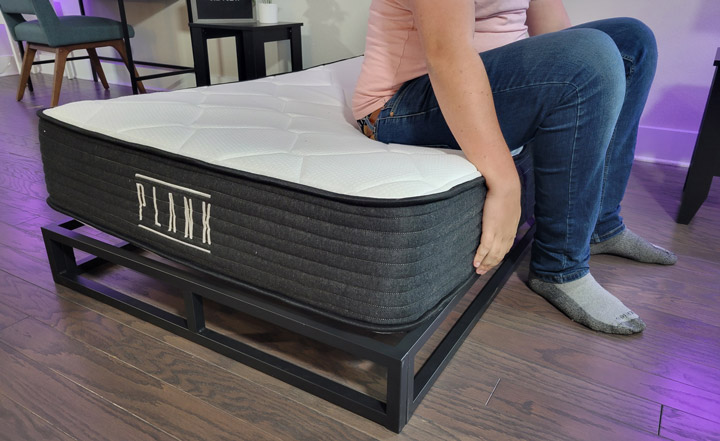 A man sits near the edge of the Plank mattress