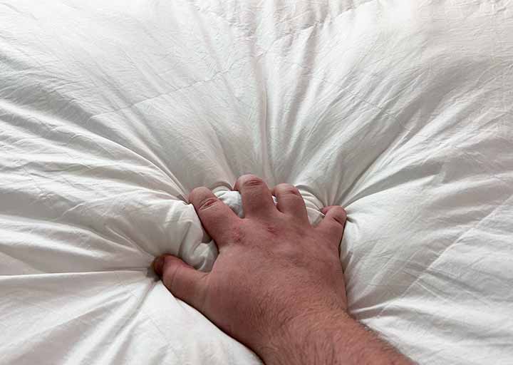 A hand squeezes the Brooklinen Down Alternative comforter to show how fluffy it is.