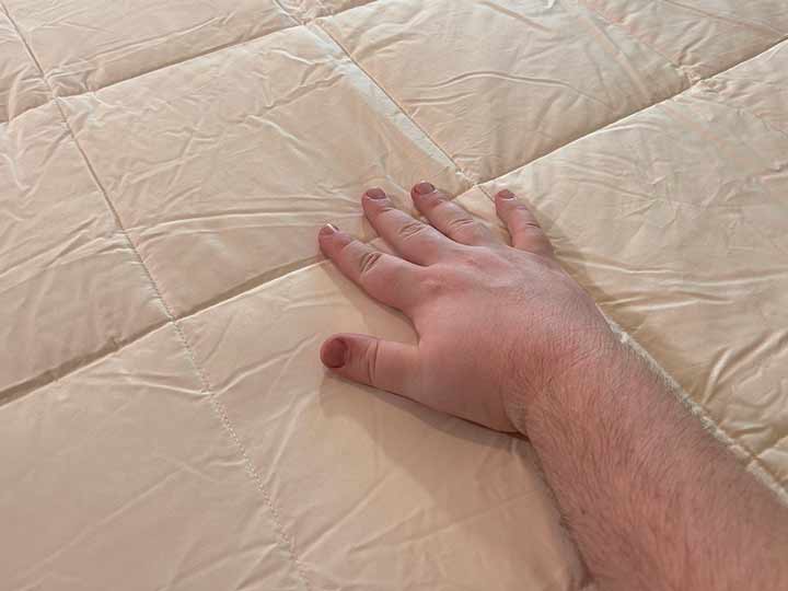 A hand runs over the top of the Nest Wool comforter.
