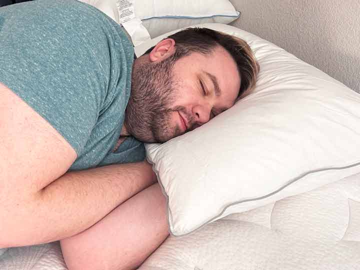 A man sleeps on his side, resting his head on the FluffCo down & feather pillow.