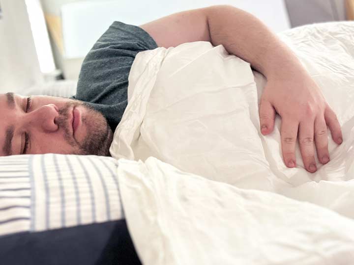 A man sleeps on his side with the Luxome Cooling Weighted Blanket draped over him.