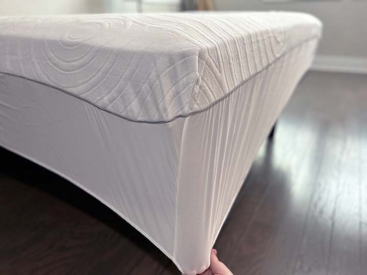 A hand pulls the corner of the TEMPUR-Protect mattress protector to show its stretch.