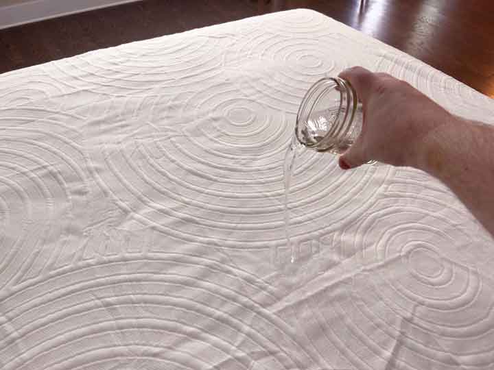 An image of a hand pouring water on top of the TEMPUR-Protect Mattress cover to show its waterproofing.