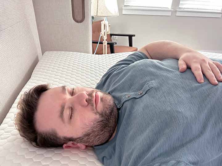 A man sleeps on his back while resting on top of the Brooklyn Bedding MIcrocoil Mattress topper.