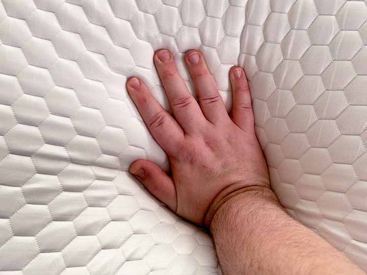 A hand pressing into the Brooklyn Bedding Microcoil Mattress topper to show off how firm it is.