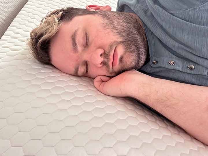 A man resting on his side while on top of the Brooklyn Bedding Microcoil Mattress Topper