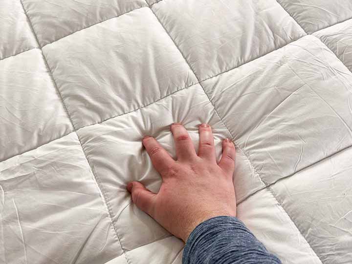A hand squeezes the top portion of the Brooklinen Mattress Topper to show its firmness and feeling.