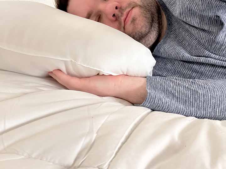 A cropped image of a man sleeping on his side while using the Brooklinen Mattress Topper.