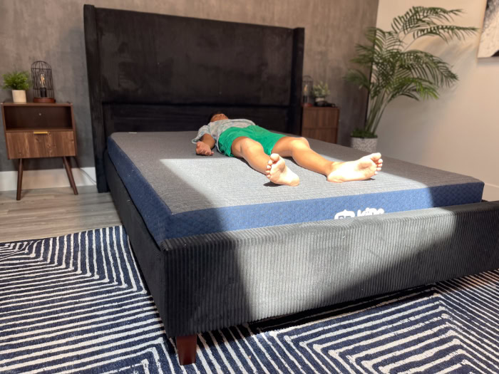 A young boy in a blue shirt and green shorts rests on his back on the Brooklyn Bedding Kids mattress