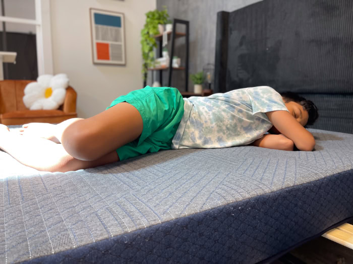 A young boy in a blue shirt and green shorts rests on his side on the Brooklyn Bedding Kids mattress