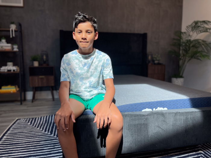 A young boy in a blue shirt sits on the Brooklyn Bedding Kids mattress