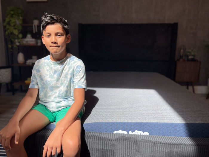 A young boy in a blue shirt sits on the Brooklyn Bedding Kids mattress