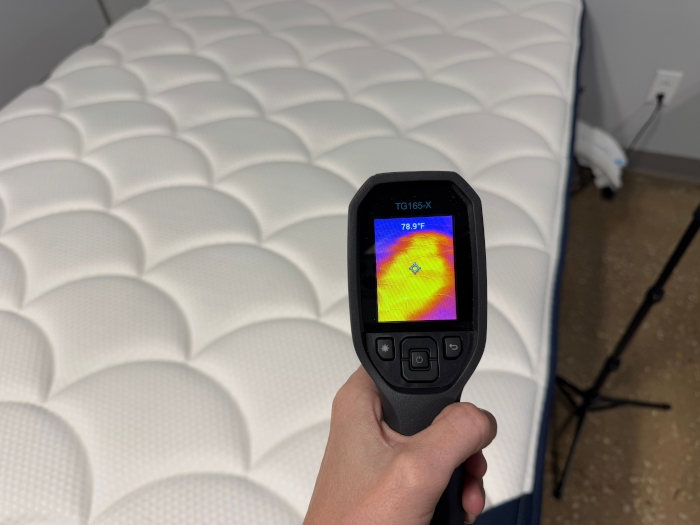 A hand holds a thermal imaging gun to assess the cooling abilities of a DreamCloud Classic Hybrid mattress.