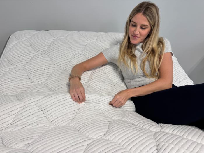 Kayla touches the cover of the DLX Classic Two-Sided Mattress while it's on an adjustable base