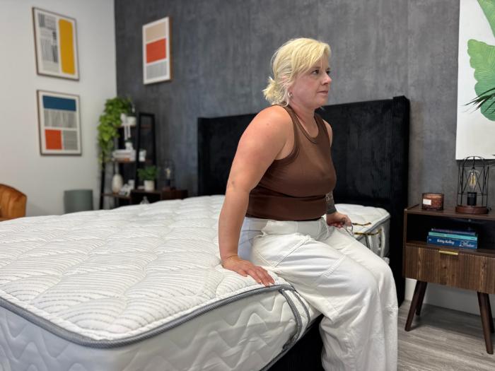 A woman sitting at the edge of the DLX Classic Two-Sided Mattress