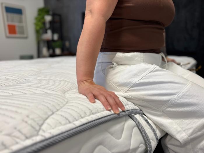 A woman sitting on the edge of the DLX Classic Two-Sided Mattress