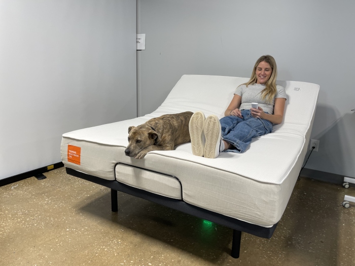 A woman laughs while lounging with a dog on a Boring Hybrid Mattress