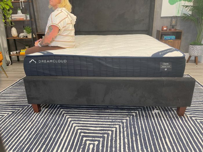 A woman sits on the edge of the DreamCloud Memory Foam mattress