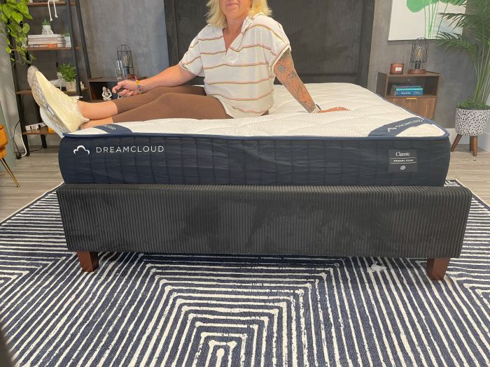A woman sits at the bottom of the DreamCloud Memory Foam Mattress