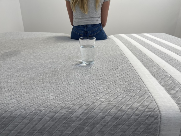 Testing motion isolation on the Leesa Original mattress by sitting on the bed near a glass of water